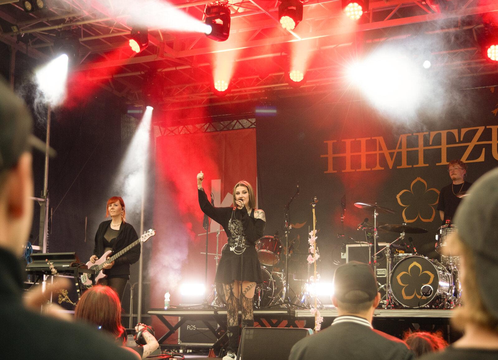 Die Band HIMITZU auf der rot ausgeleuchteten Bühne, Sängerin und Bassistin vor dem Publikum