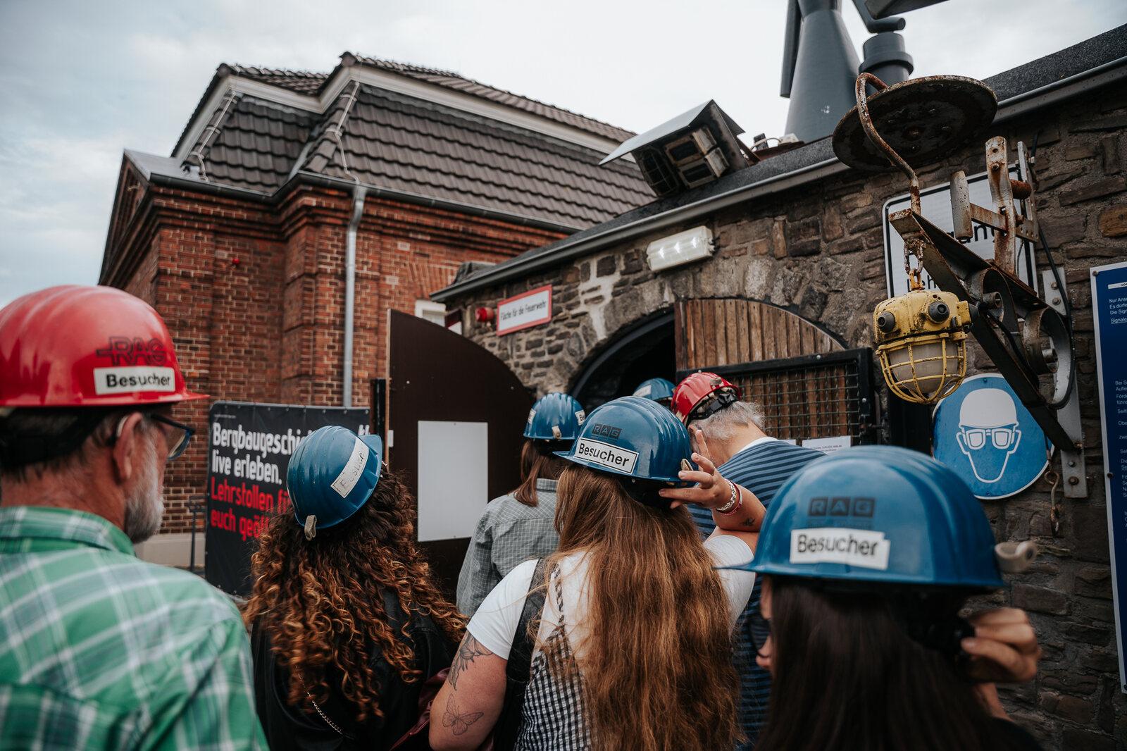 Besucherinnen und Besucher mit Schutzhelmen bei einer Führung vor dem historischen Ziegelgebäude des Schirrhofs