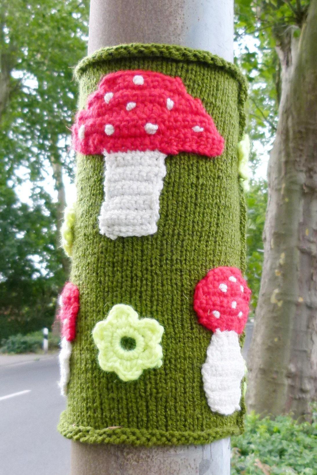 Umstrickter Laternenmast mit gehäkelten Fliegenpilzen und Blüte