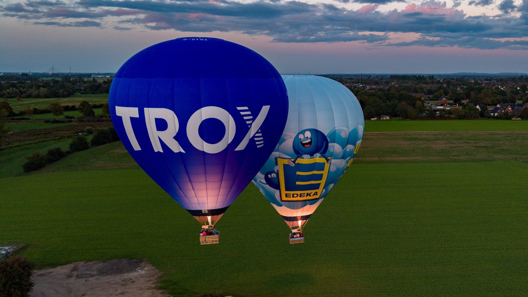 Heißluftballons von TROX und EDEKA in der Abenddämmerung über einer Wiese am Niederrhein