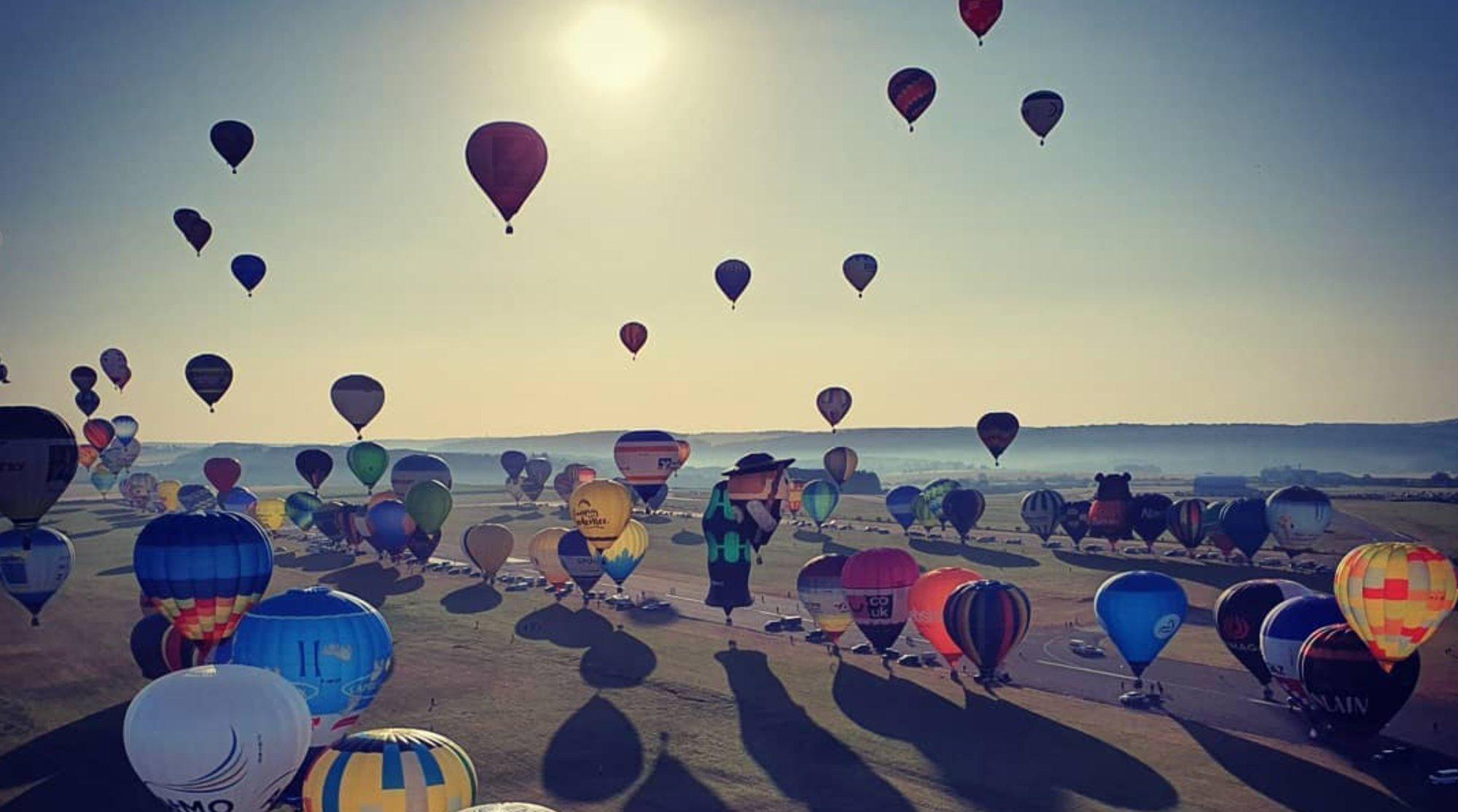 Zahlreiche Heißluftballons beim Massenstart vor der tiefstehenden Sonne