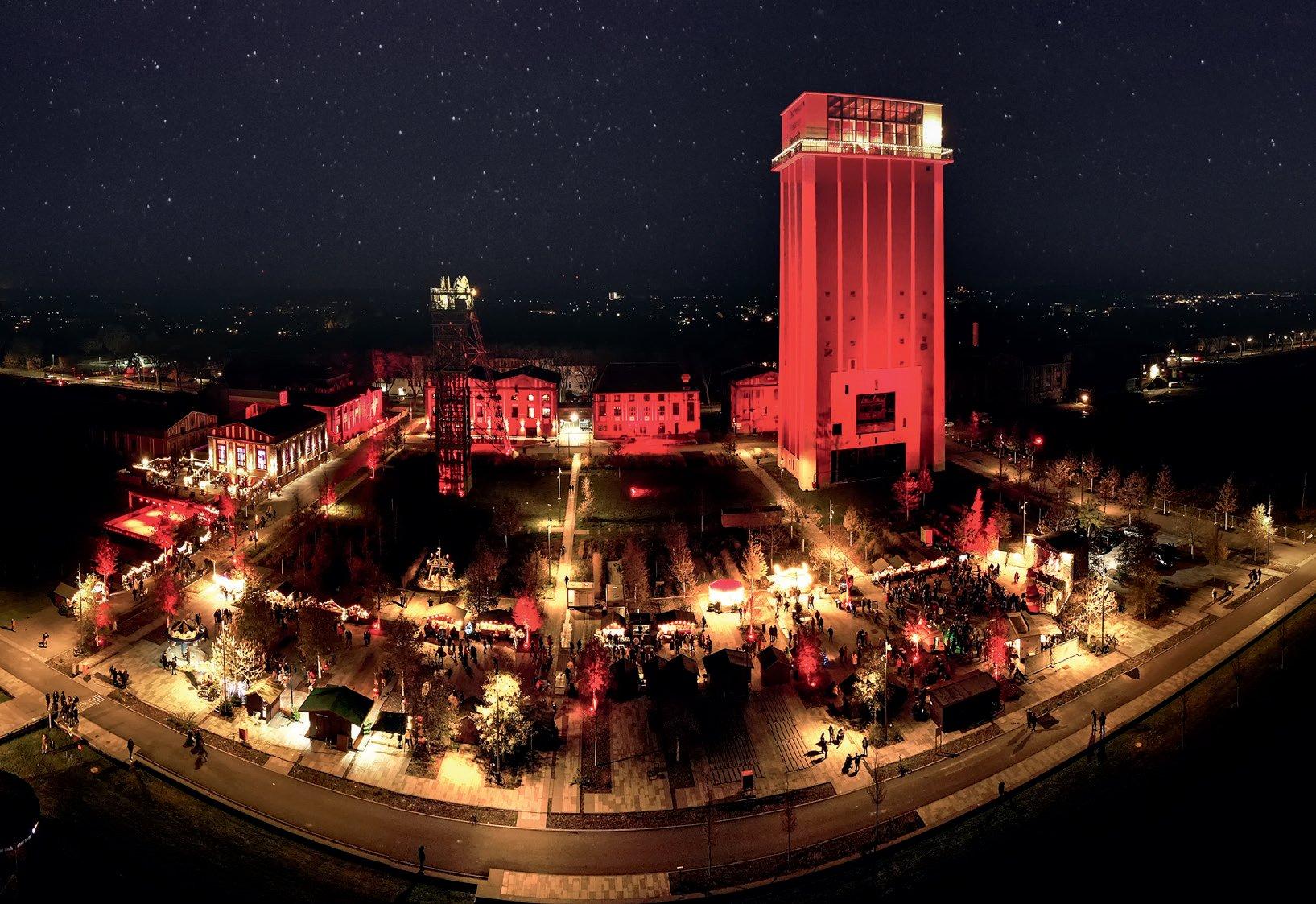 Rot beleuchteter Zechenturm bei Nacht über dem Weihnachtsmarkt im Zechenpark