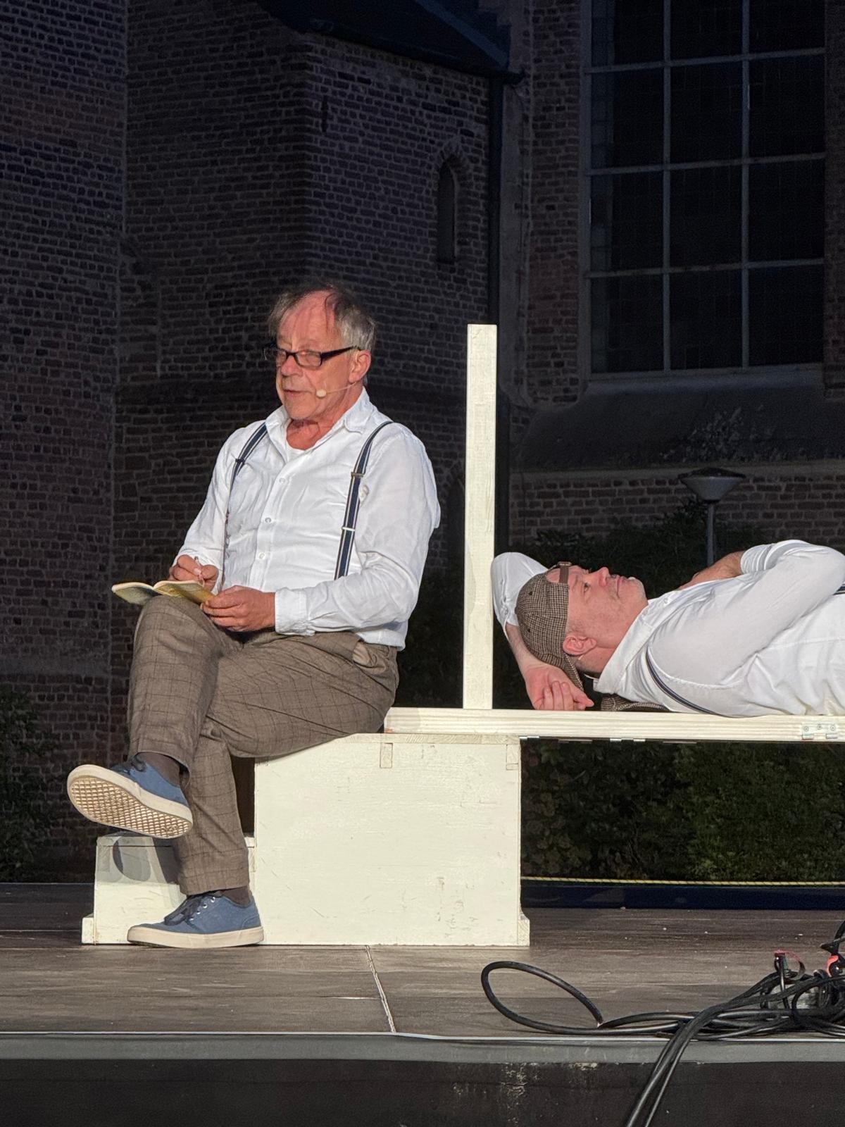 Darsteller sitzt lesend auf einer Stufe, ein zweiter liegt daneben