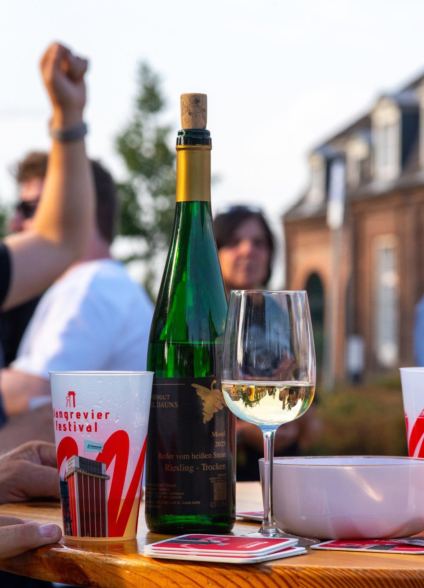 Tisch mit Weinflasche, Glas und klangrevier-Bechern vor dem Schirrhof