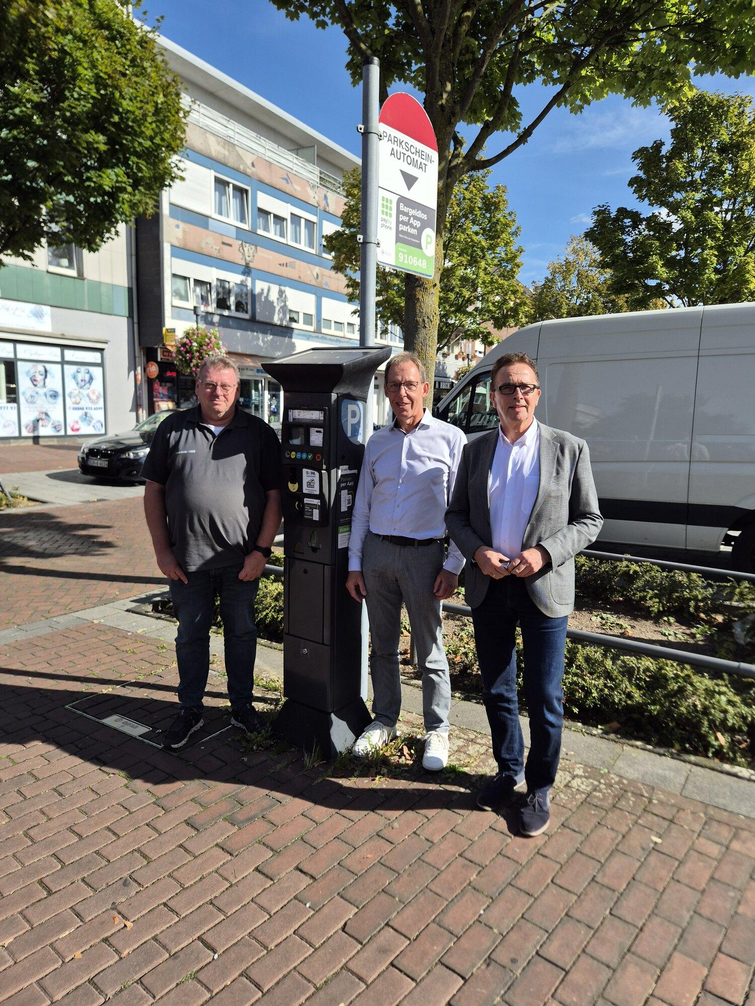 Drei Vertreter von Von Herzen Kamp-Lintfort stehen an einem Parkscheinautomaten in der Innenstadt