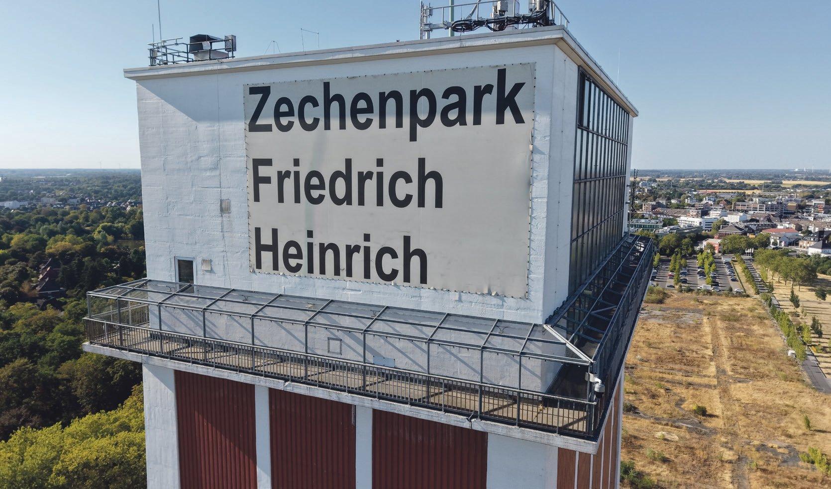 Luftaufnahme des Zechenturms mit der Aufschrift „Zechenpark Friedrich Heinrich“ und Aussichtsplattform, dahinter der Zechenpark und Kamp-Lintfort