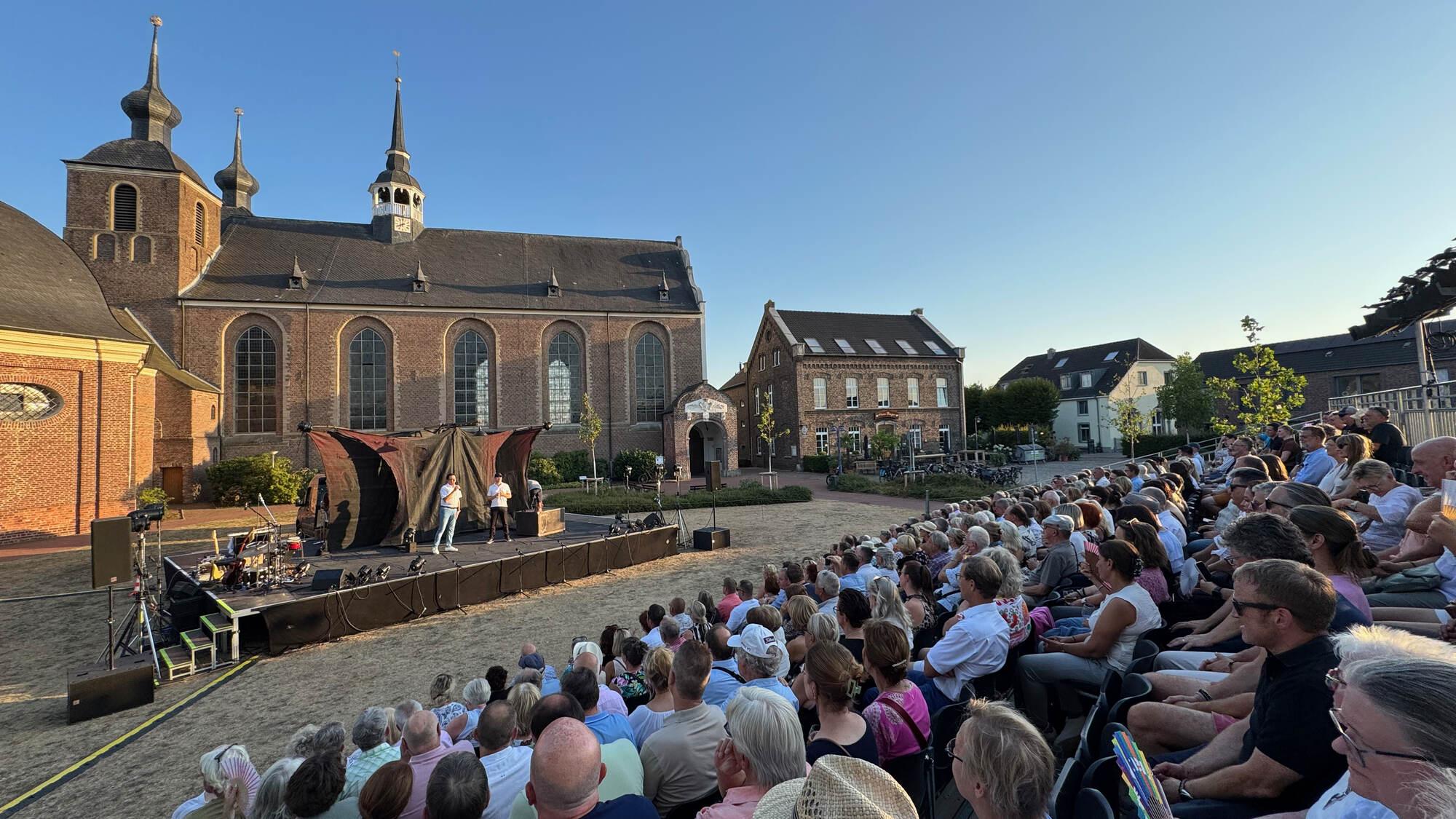 Blick von hinten über das voll besetzte Publikum auf die Bühne des Kamper Freilichttheaters vor dem Kloster Kamp